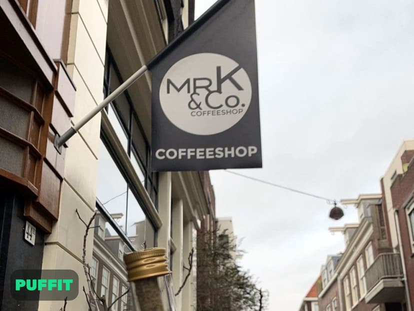 שלט התלייה של מיסטר קיי עם הלוגו MR K & Co. בולט מעל הרחוב בצילום מלמטה